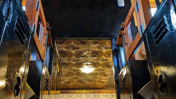 Un ascenseur luxueux, avec un intérieur raffiné, un plafond orné de motifs dorés et un mur recouvert de miroirs.