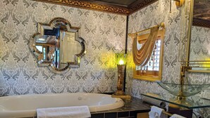Une salle de bain avec une grande baignoire, un miroir doté d’un cadre décoratif, un meuble-lavabo avec un vasque en verre et un papier peint à motifs.