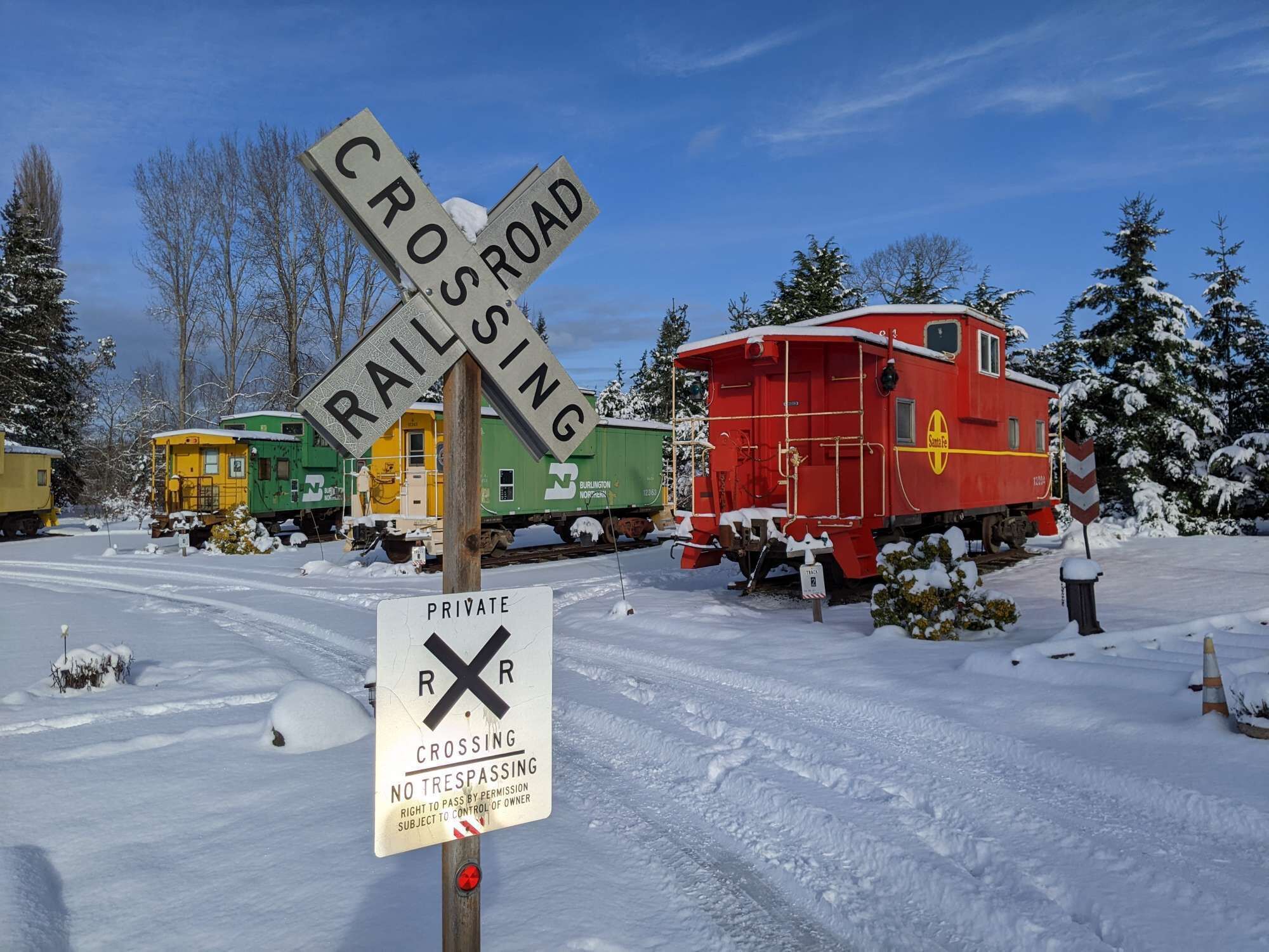 A snow-covered railroad crossing with a red caboose and green train cars.