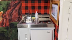 Une petite cuisine équipée avec des meubles blancs, un évier en acier inoxydable et un four à micro-ondes.