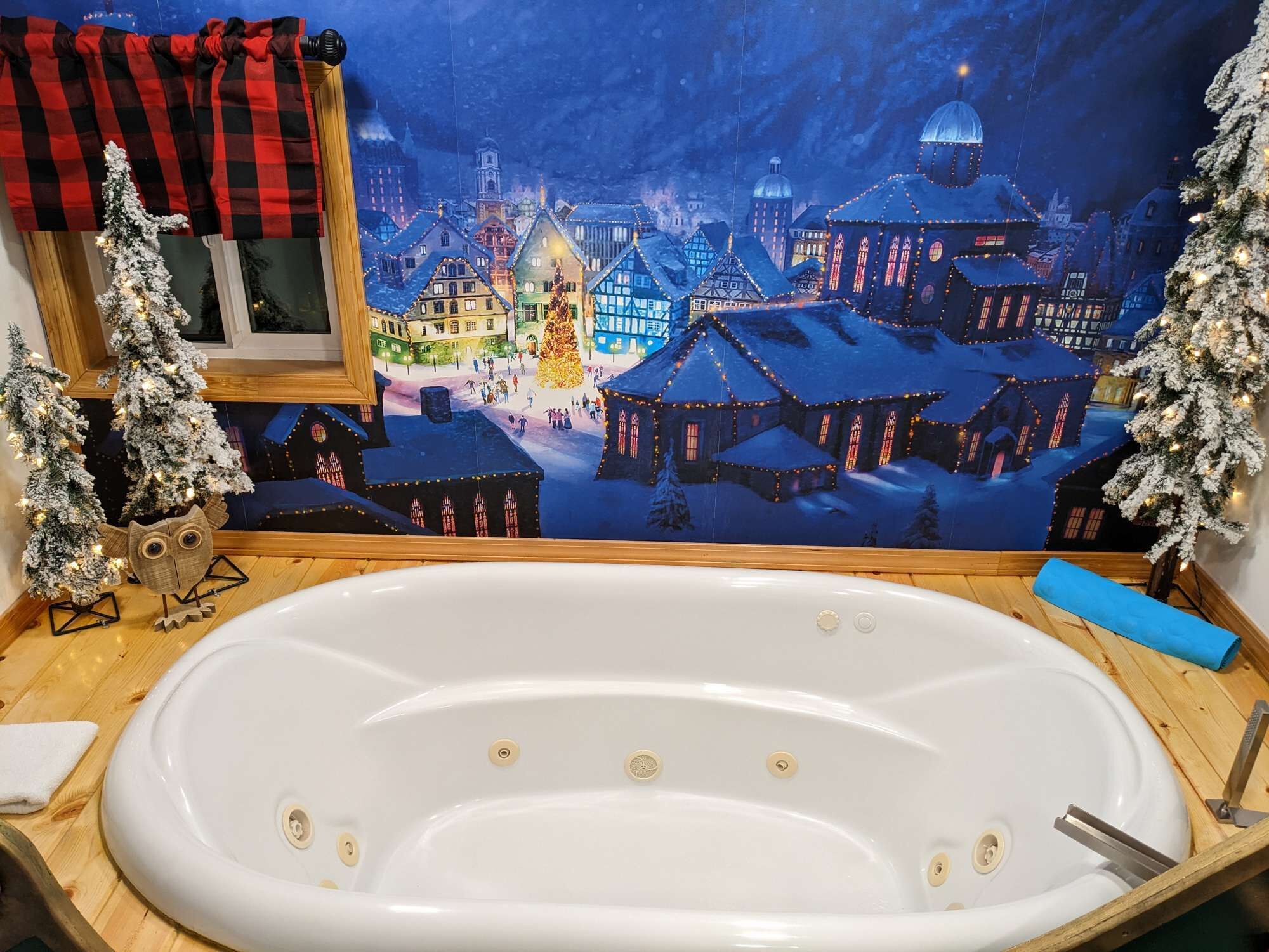 Ein Badezimmer mit einer großen weißen Badewanne, Holzboden und einem stimmungsvollen Wandgemälde eines verschneiten Dorfes.