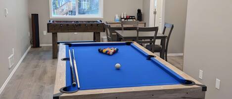 A pool table in a room with a window, a coffee machine, and a door.
