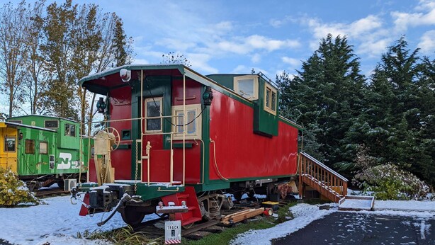 Un wagon de train immobile, de couleur verte et rouge, est garé sur des rails, et une rampe en bois mène à sa porte.