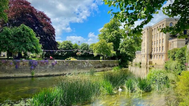Een vredig rivierlandschap met een historisch gebouw, weelderige begroeiing en een heldere lucht.