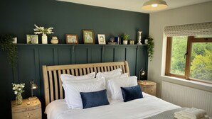 Een keurig opgemaakt slaapkamer met een houten bed, witte beddengoed, een bedlampje en een raam met uitzicht op groen.