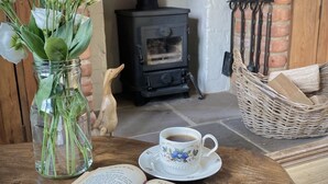 Een gezellige kamer met een open haard, een bloevas, een kop koffie en een boek open op een houten tafel.