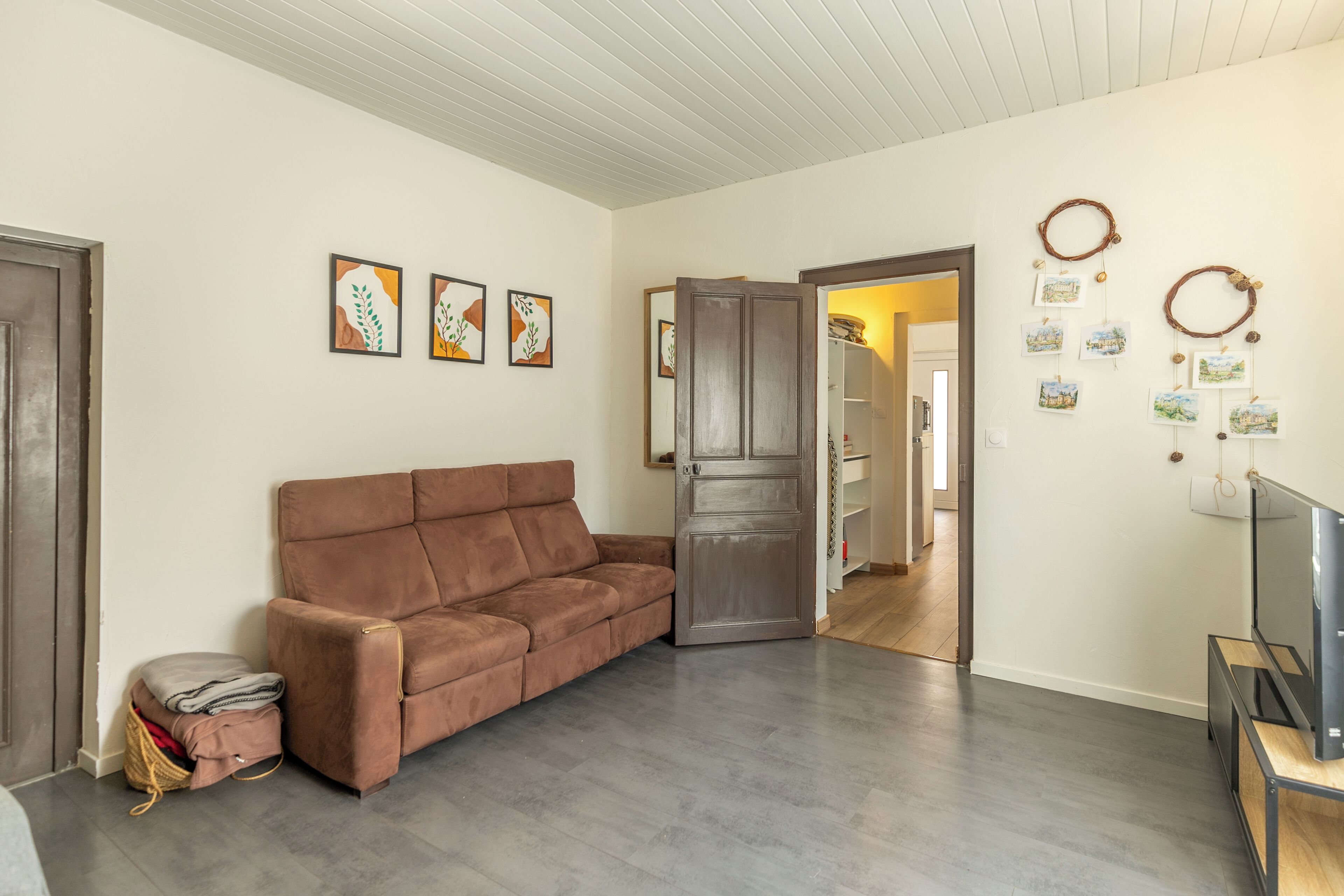 Ein Wohnzimmer mit braunem Sofa, einem Fernseher auf einem Schrank und einem Holzkabinett.