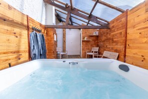 A wooden cabin with a hot tub, wooden walls, and a small seating area. - La Maisonnette bien-être (Bagneux)