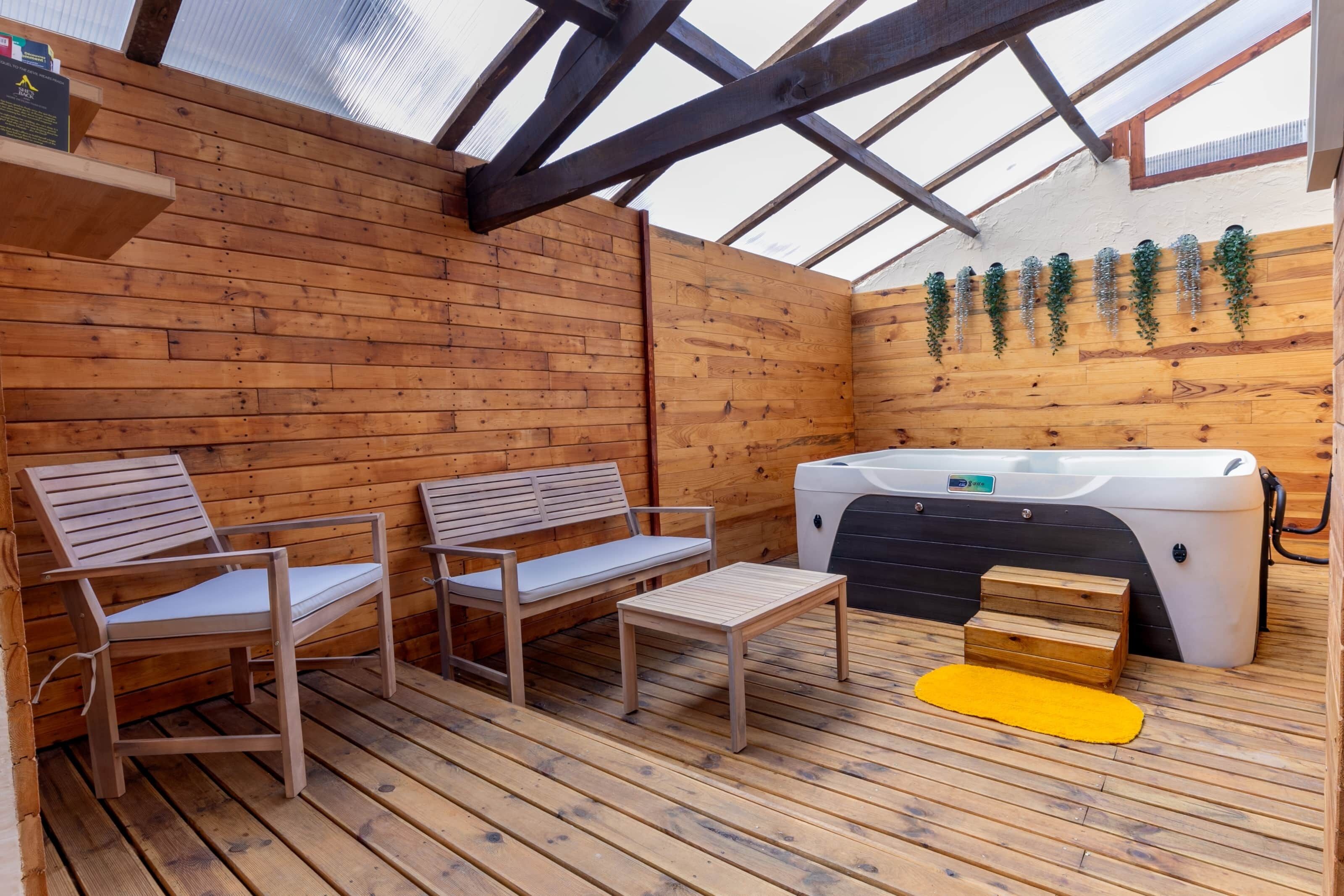 A wooden deck with two wooden chairs and a small table, a hot tub, and wooden steps.