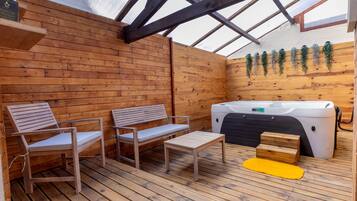 A wooden deck with two wooden chairs and a small table, a hot tub, and wooden steps.