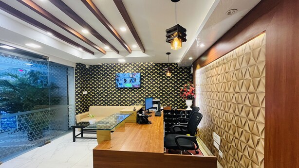 A modern reception area with a wooden reception desk, black office chairs, a glass partition, and a patterned wall. - HOTEL ROYAL PARK (Chennai)