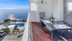 En balkon med udsigt over havet, et spisebord dækket med glas og en flaske, samt en stol.