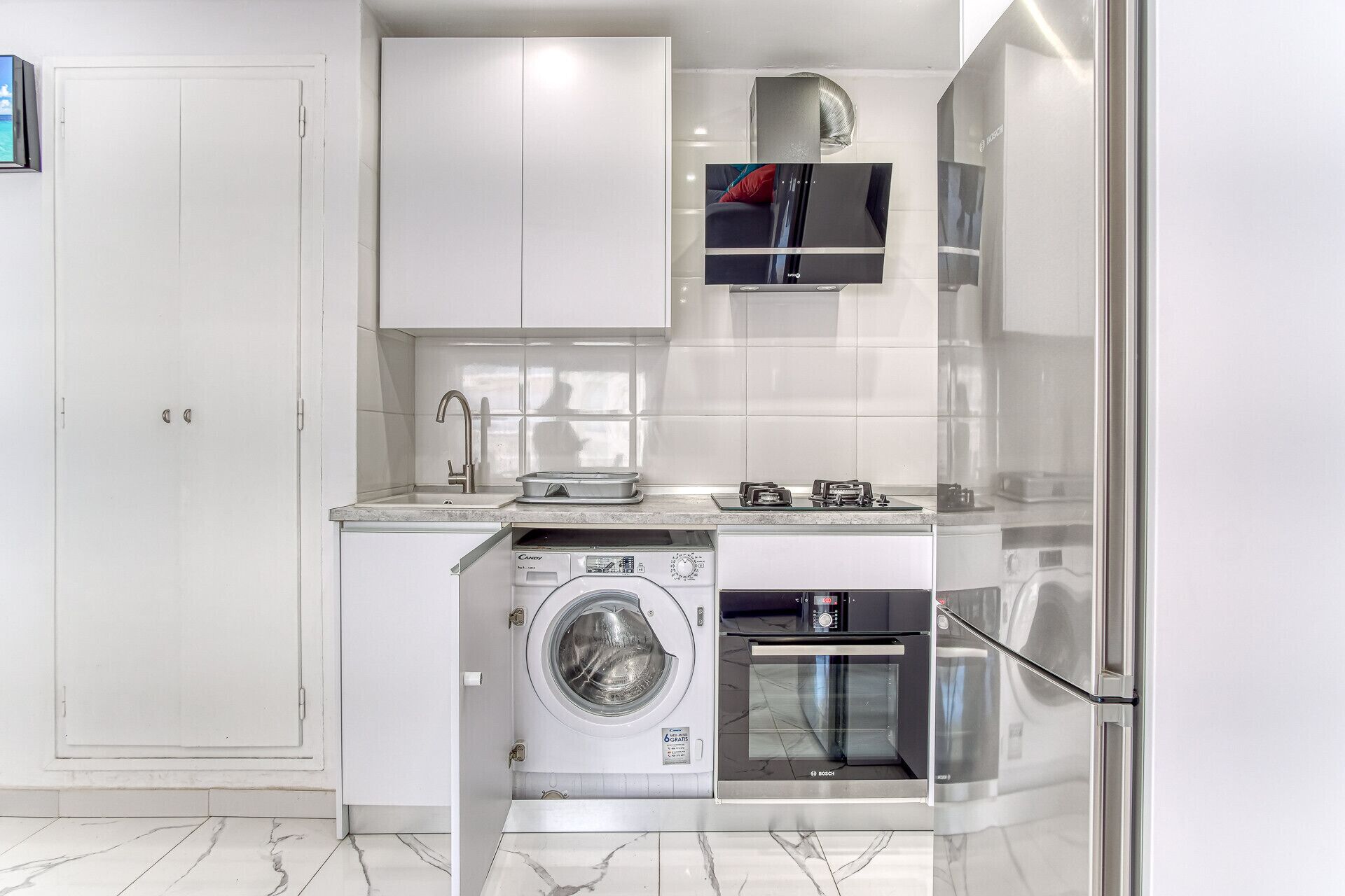 A modern kitchen with a built-in washing machine, a Bosch oven, and a flat-screen TV mounted above the stove.