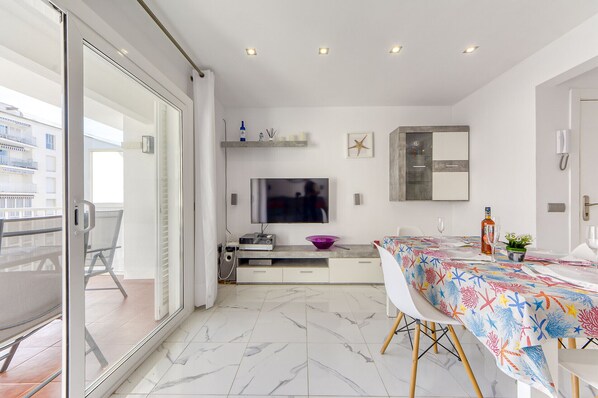 Una cocina moderna con comedor, un televisor montado en la pared y un balcón con una silla.