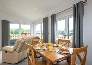 Un comedor con una mesa lista para el desayuno, un sofá y ventanas grandes con cortinas.