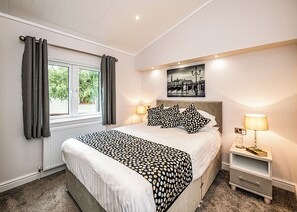 A bedroom with a bed, a nightstand, a lamp, a window with curtains, and a picture on the wall.