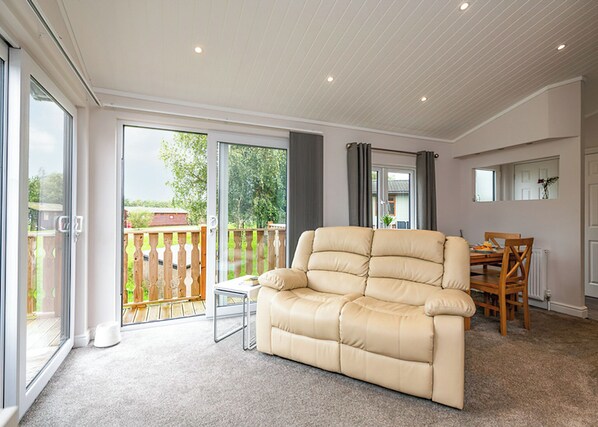 A spacious living area with a beige sofa, a dining table with chairs, and a sliding glass door leading to a balcony.