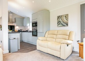 A modern kitchen with white cabinets, a built-in oven, and a dining area with a beige sofa.