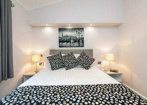 Une chambre d’hôtel avec un lit, deux lampes de chevet, une table de chevet, un tableau accroché au mur et une couvre-lit à motifs.