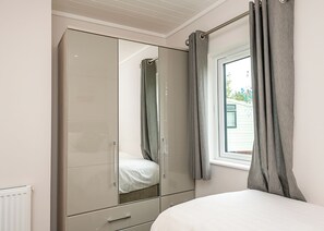 Quarto com guarda-roupa, cama, janela com cortinas e radiador.