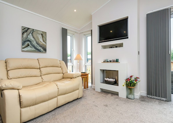 Una sala de estar con un sofá beige, un televisor de pantalla plana sobre la chimenea y un ventanal grande.