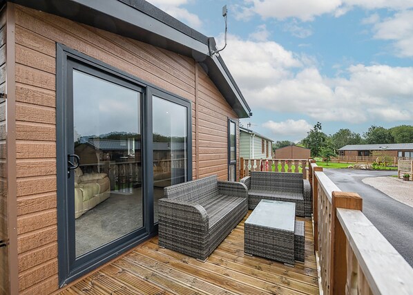 A wooden deck with outdoor furniture, a sliding glass door, and a view of the surrounding area.