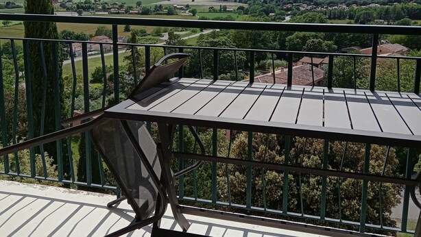 A balcony with a view of a rural landscape, including fields and distant hills.