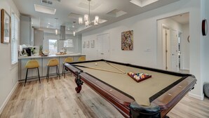 Een pooltafel in een goed verlichte ruimte met een bar, stoelen en kunstwerken aan de muren.