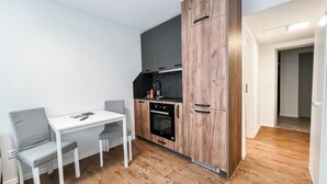 Eine kompakte Küche mit weißem Tisch und Stühlen, einem eingebauten Ofen und einer grauen Spritzschutzwand.