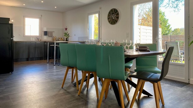 A modern kitchen with a dining area, featuring a large window, a clock, and a dining table set with chairs.