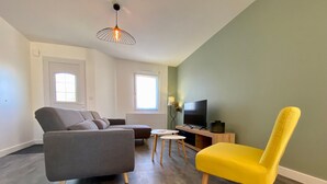 A modern living room with a grey sectional sofa, a yellow armchair, a small white table, and a TV on a wooden stand.