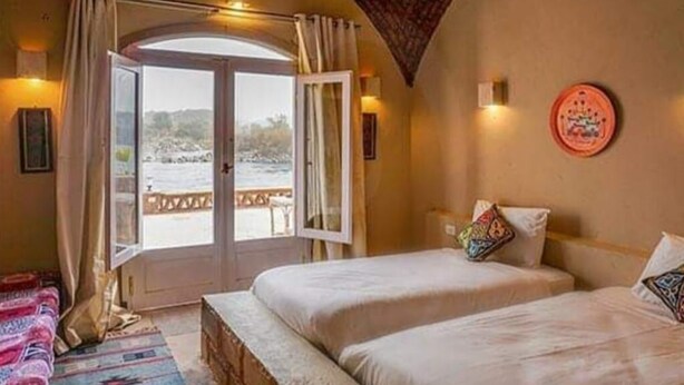 Un dormitorio con dos camas, vista al mar a través de una puerta abierta y un adorno redondo en la pared.
