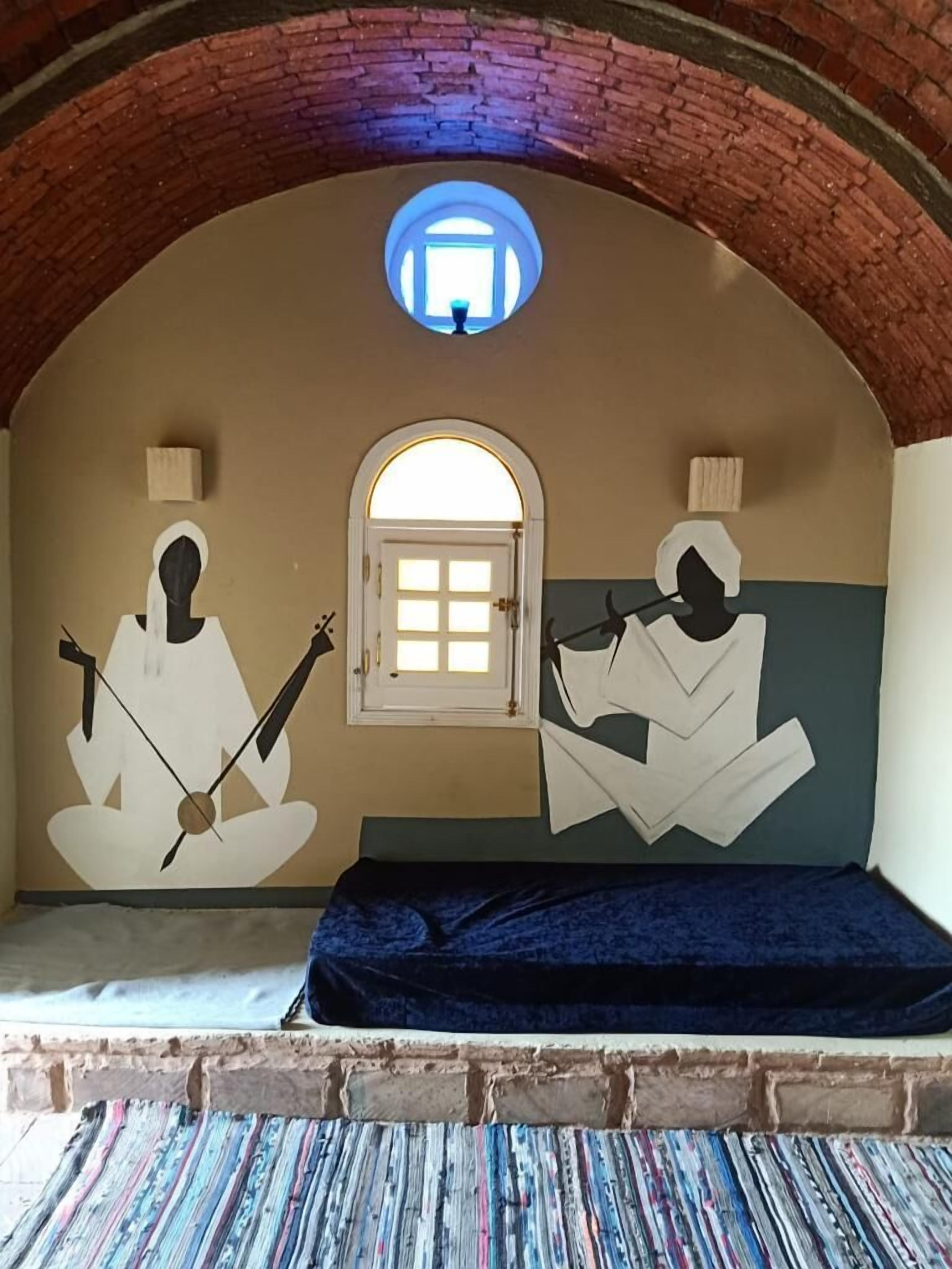 A room with a brick arch ceiling, a small window, and a bed with a blue mattress.