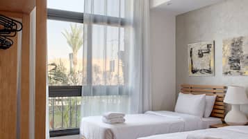 Una habitación de hotel moderna con dos camas, un armario de madera, un ventanal con cortinas translúcidas y una obra de arte en la pared.