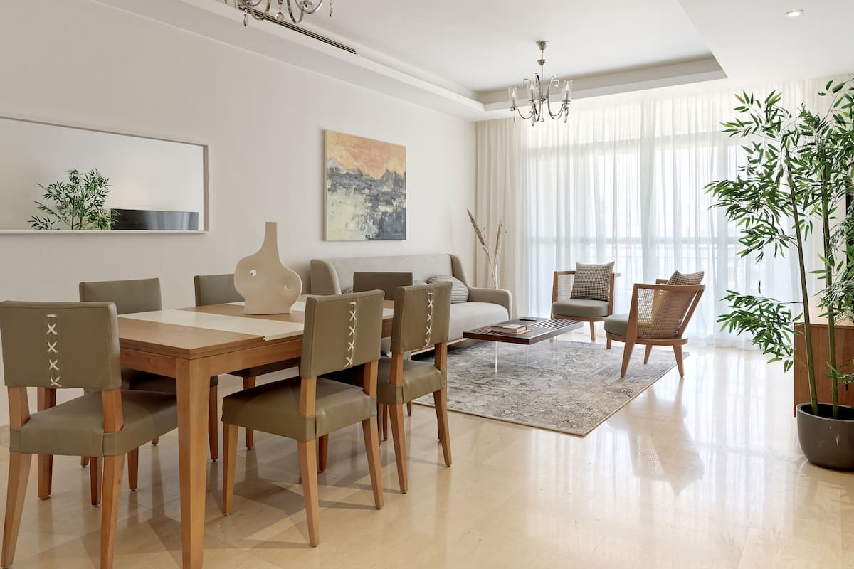 A modern living room with a dining area, featuring a wooden dining table, matching chairs, a sofa, and a large potted plant.