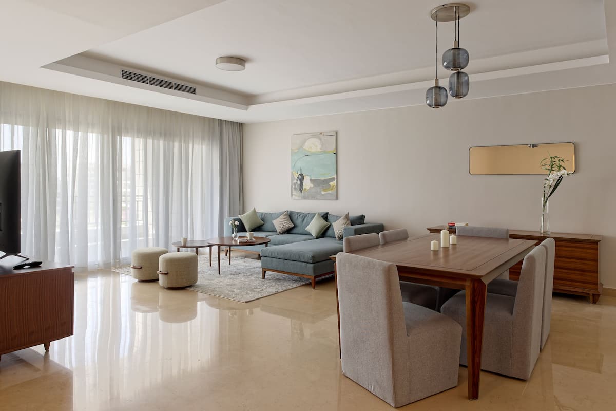 A modern living room with a sofa, dining table, and chairs, a TV, and artwork on the wall.