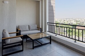 A balcony with a sofa and a coffee table, a view of a residential area, and a railing. - VESTA - Cairo Festival City Residence (New Cairo)