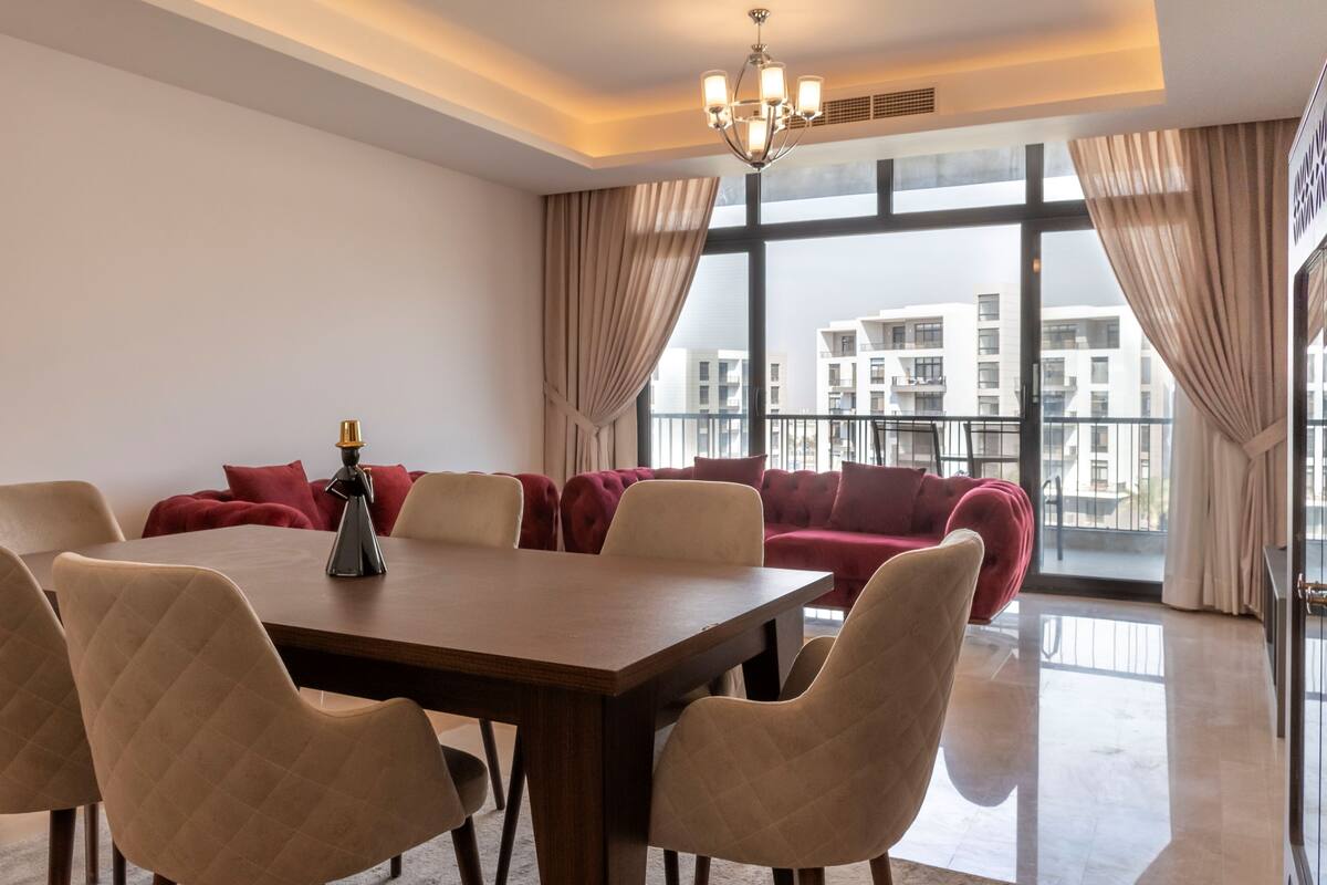 A modern living room with a dining area, large windows, and a view of buildings.