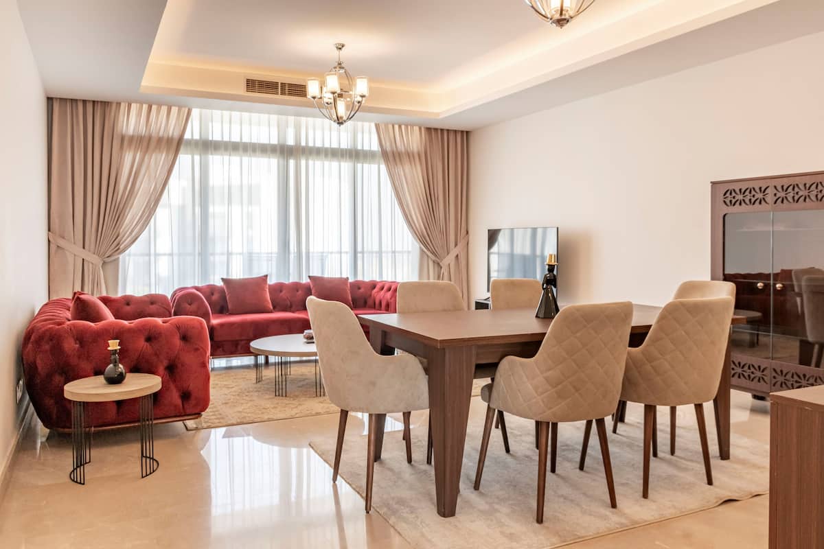 A modern living room with a red sofa, a dining table with chairs, and a large window with curtains.