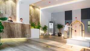 A modern reception area with a wooden reception desk, potted plants, and a seating area with a bench. - Areca Hotel (Yangon)