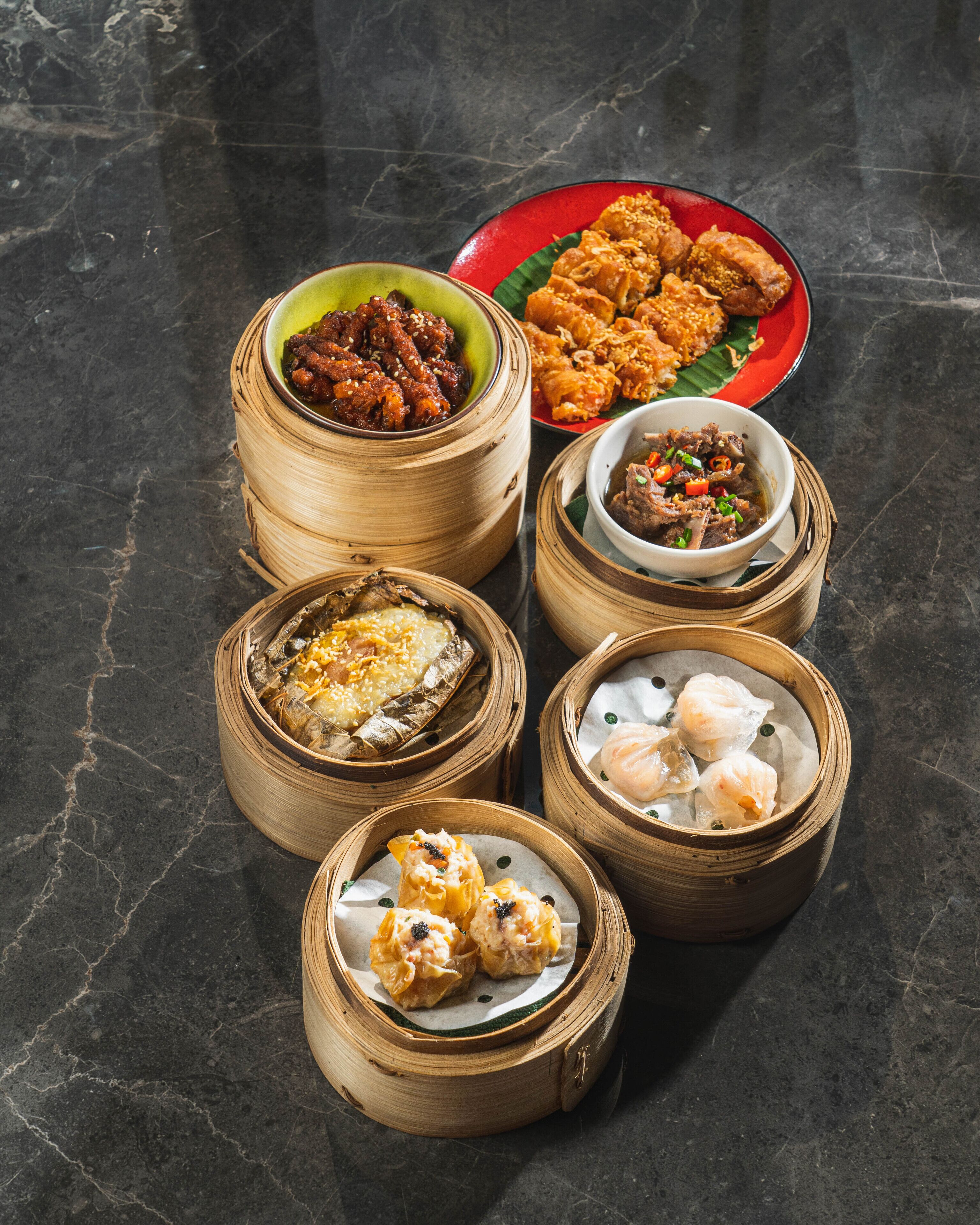 A variety of dim sum dishes in bamboo steamers on a dark marble surface.