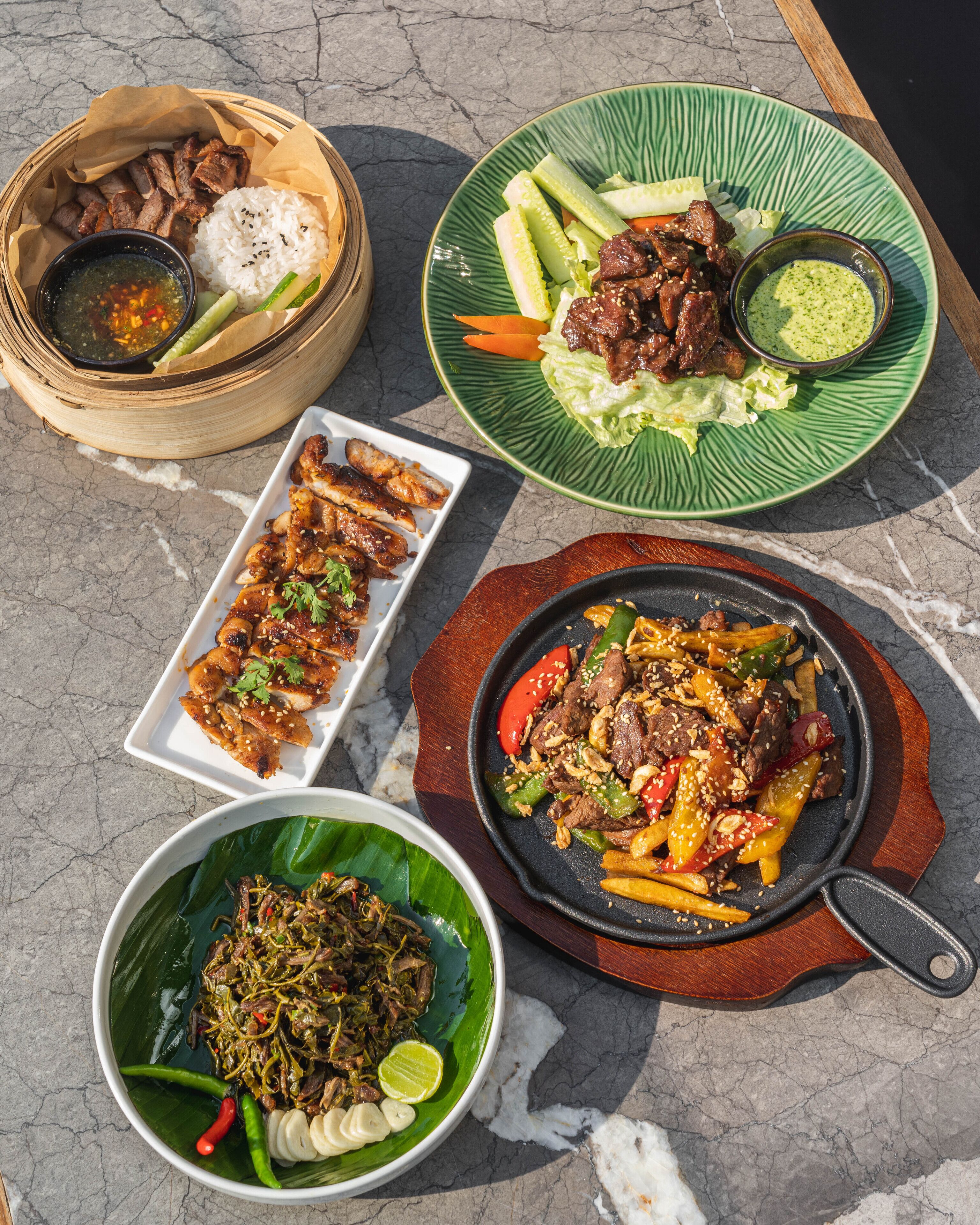 Diversos platos, como carne a la parrilla, arroz y verduras, sobre una mesa de mármol.