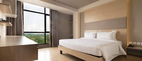 A modern hotel room with a large bed, a desk, and a view of the city through large windows.