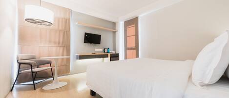 Una habitación de hotel moderna con una cama grande, un escritorio con un televisor de pantalla plana, una silla y una lámpara colgante.