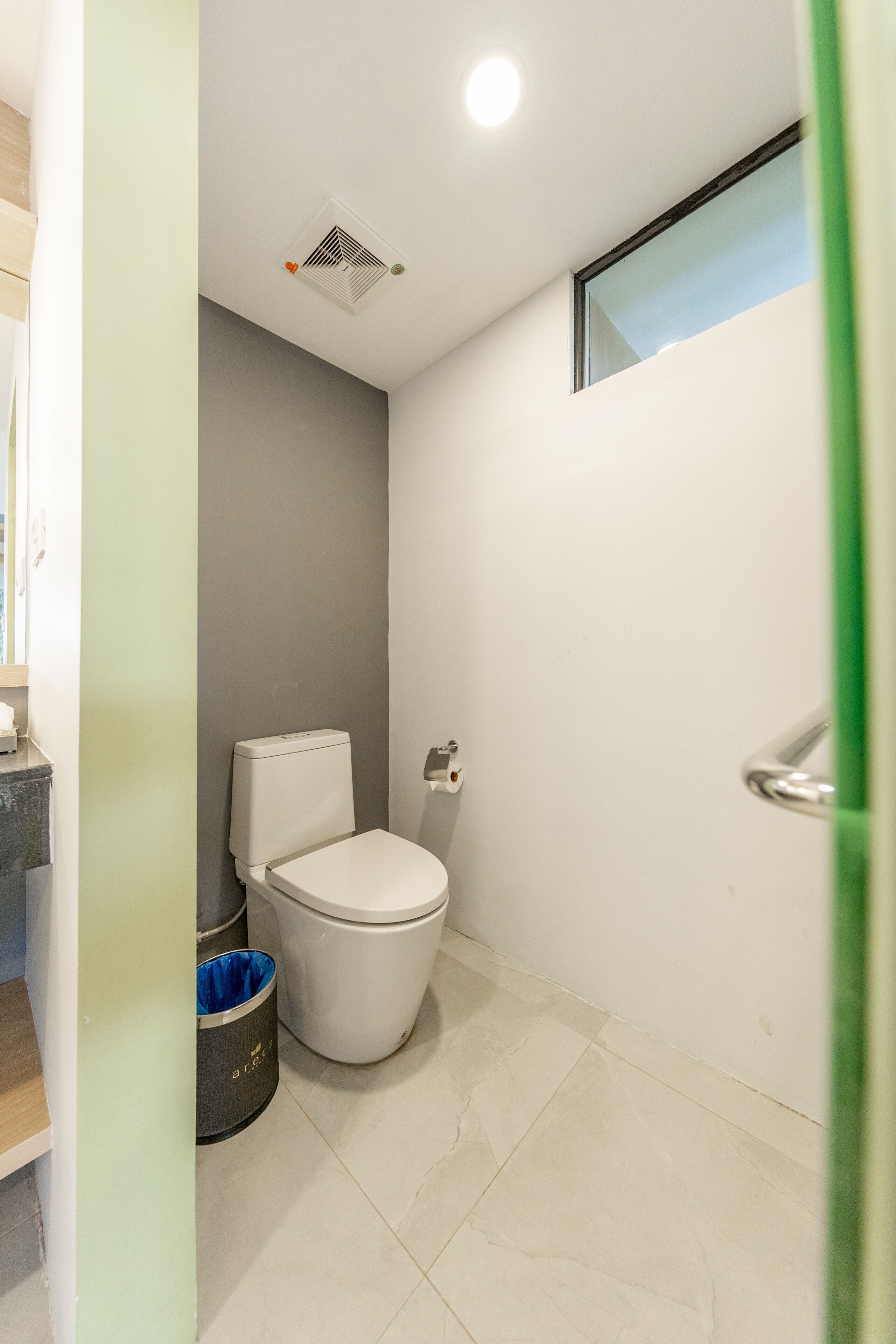 A small, clean bathroom with a toilet, a trash bin, and a window.