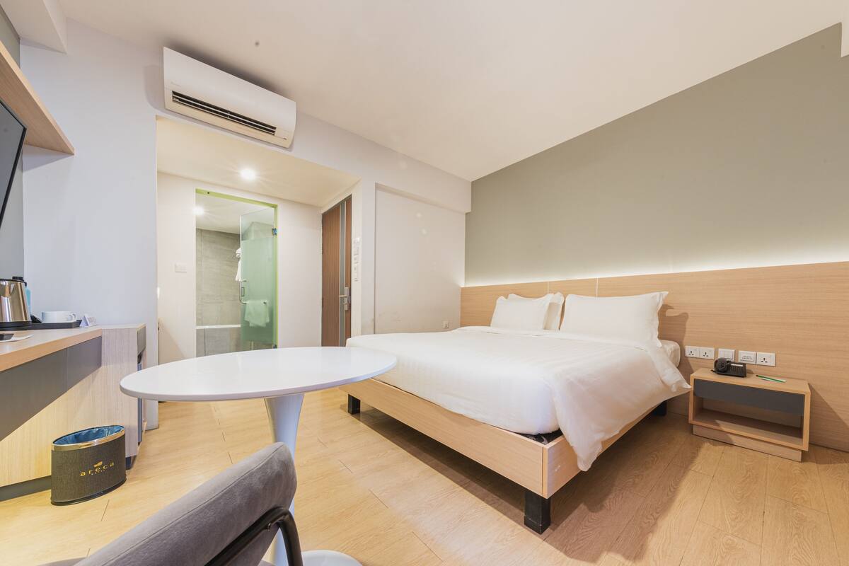 Una habitación de hotel moderna con una cama, una mesita de noche y una pequeña zona de escritorio con una silla.