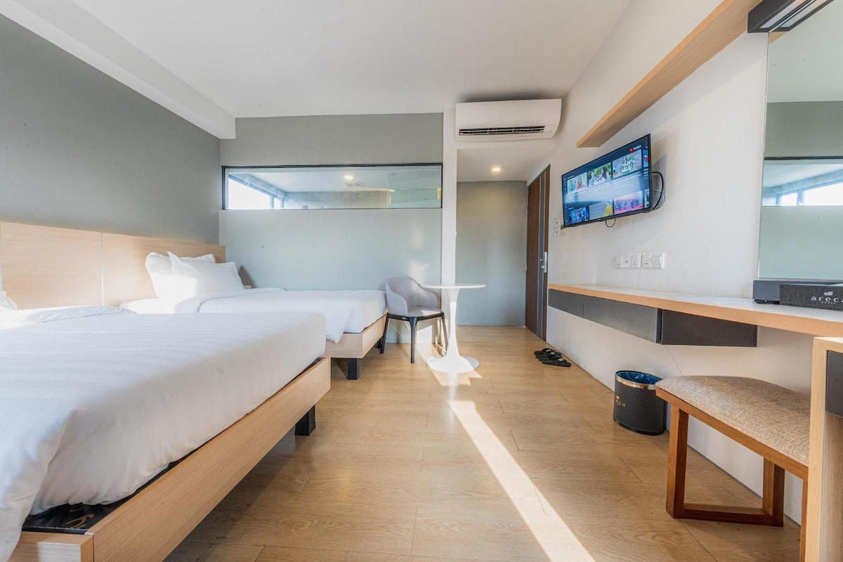 A hotel room with two beds, a desk, a chair, a TV, and a trash bin.