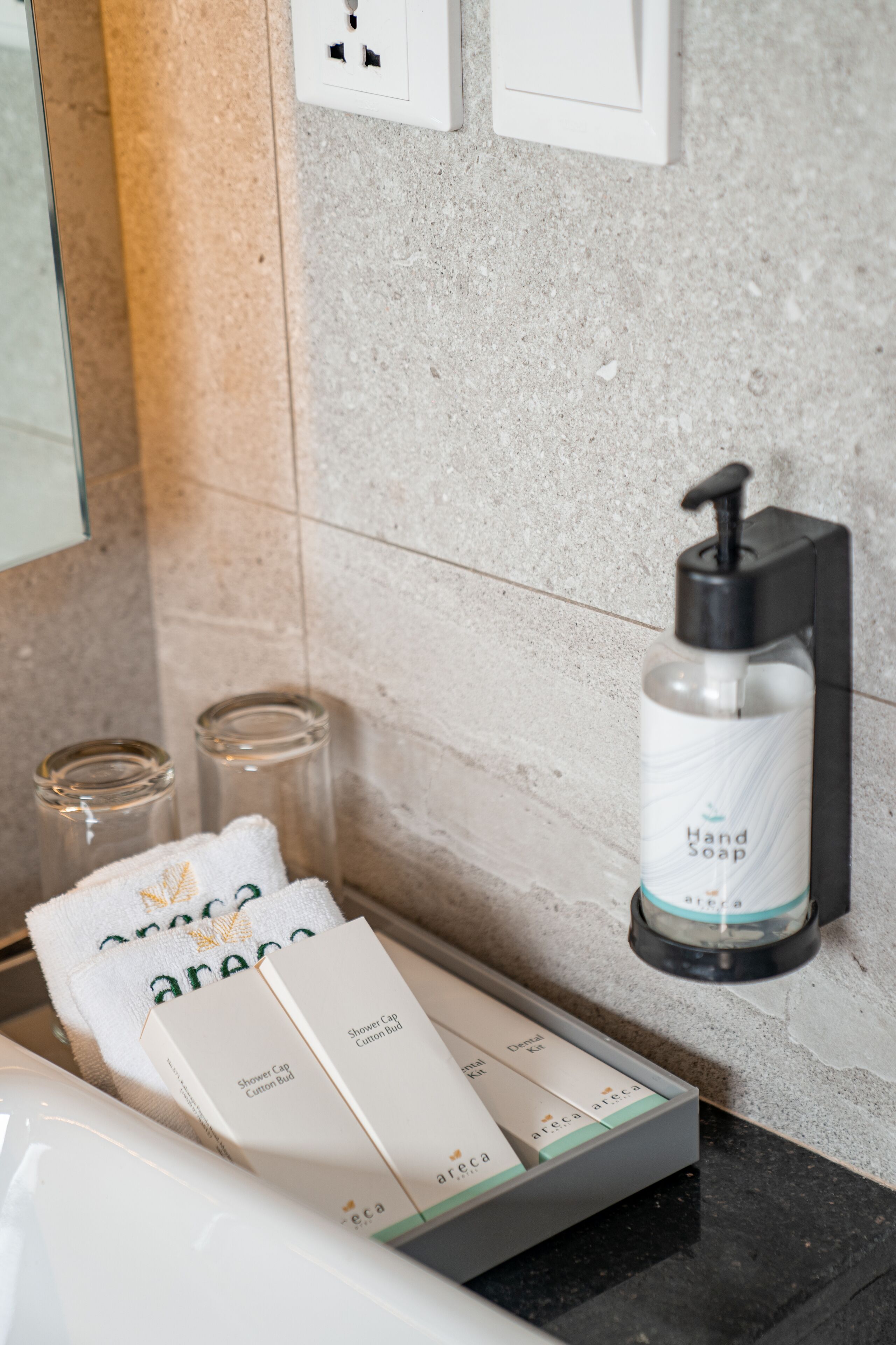 A bathroom with a hand soap dispenser, a towel, and a box of shower cap and cotton bud.