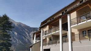Un edifici de diverses plantes amb balcons, un vestíbul cobert i vista a un paisatge de muntanya.