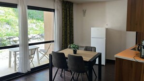 Una cuina compacta amb nevera, una taula de dinar amb caires i vista a la vegetació exterior.